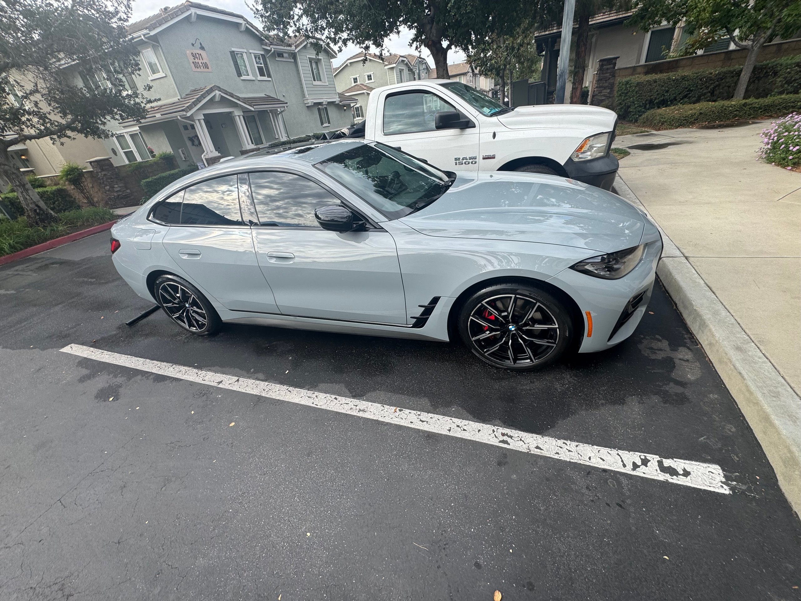 Silver BMW sedan parked on street with white truck in residential neighborhood