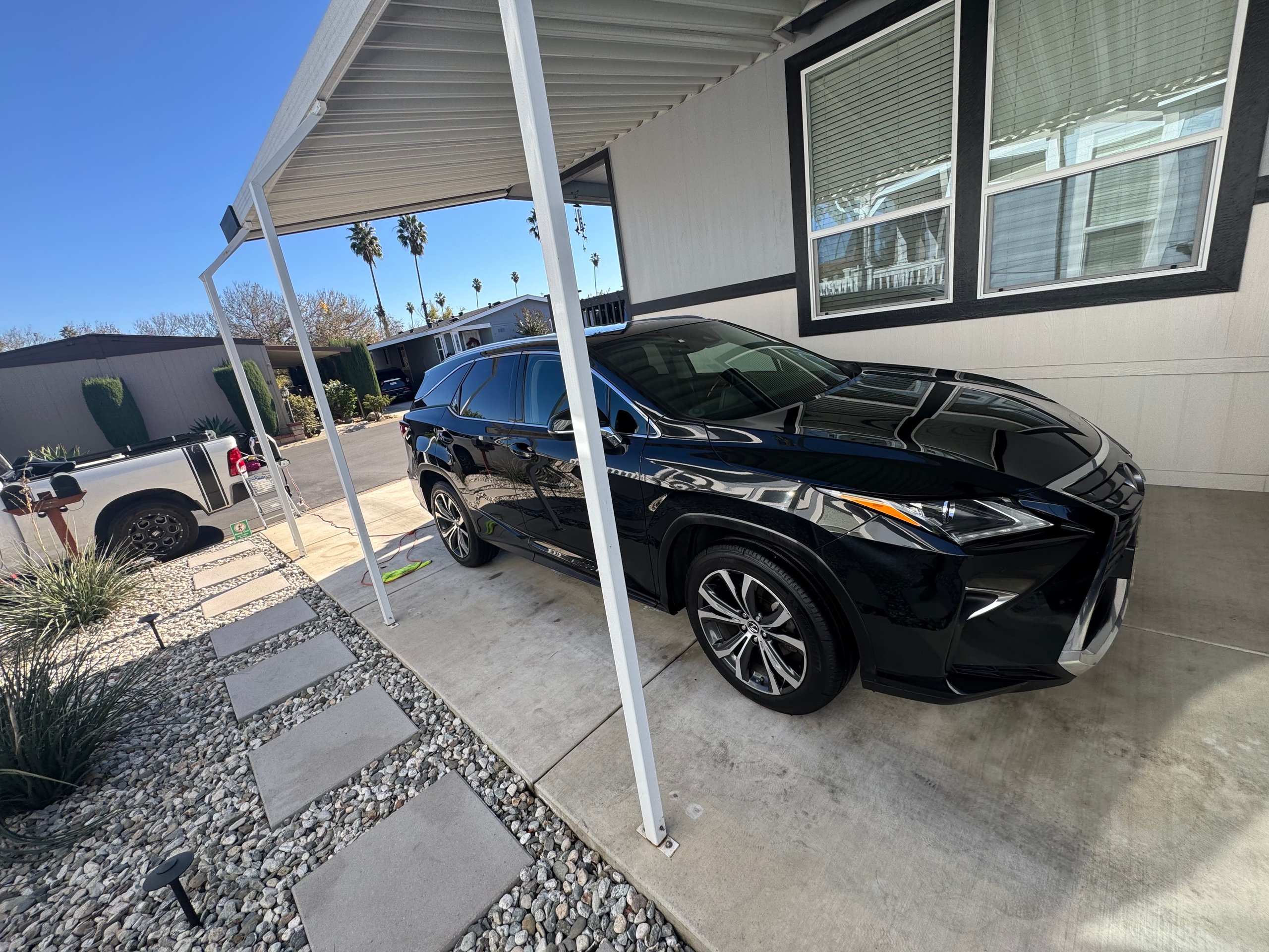 Black SUV parked under carport with palm trees in background