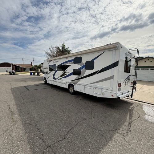 Large white RV parked on asphalt street with cloudy sky background