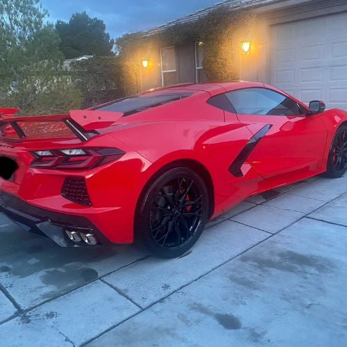 Bright red sports car parked in driveway at dusk with garage lights